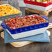 A blue and white Tuxton rectangular casserole dish with food in it.