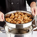 A person holding a Vollrath stainless steel food container filled with food.