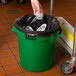 A hand putting foil in a Lavex green round trash can.