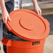 A person holding a Lavex orange plastic lid over a garbage can.