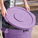 A person holding a Lavex purple round commercial trash can lid