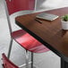 A square reversible walnut and oak table with a black edge, paired with a red metal chair and a 30-inch cast iron base.