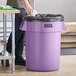 A man in black gloves putting a black plastic bag in a purple Lavex round commercial trash can.