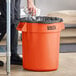 A man putting a black liner in an orange Lavex trash can.