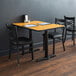 A Lancaster Table & Seating table with a reversible walnut and oak top and cast iron base plates on a wood floor with black chairs.