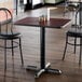 A square standard height restaurant table with a reversible cherry and black top and a black cast iron base.