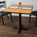 A Lancaster Table & Seating table with a 30" x 30" reversible walnut and oak table top and a cross cast iron base plate.