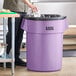 A man standing next to a Lavex purple round commercial trash can.