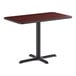 A rectangular standard height table with a reversible cherry and black top and a black cross cast iron base.