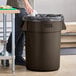 A man standing next to a Lavex brown round commercial trash can.
