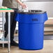 A man standing next to a Lavex blue round commercial trash can.