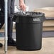 A man putting trash in a black Lavex trash can.