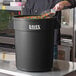 A man standing in front of a Lavex black round trash can full of colorful sprinkles.