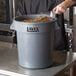 A chef pouring candy into a Lavex gray plastic bin.