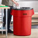 A man putting a black plastic bag in a red Lavex 55 gallon round trash can.