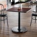 A square restaurant table with a reversible cherry and black top, supported by a round cast iron base.