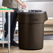 A man standing next to a Lavex brown plastic trash can.