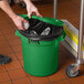 A person's hands putting foil in a green Lavex round commercial trash can.