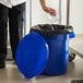 A woman using a blue Lavex Commercial trash can to recycle a plastic cup.