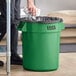 A man putting a black plastic bag in a green Lavex 20 gallon trash can.