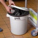 A person putting foil in a Lavex white round trash can with a lid.