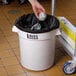 A hand putting foil in a white Lavex commercial trash can with a black bag inside.