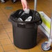 A hand putting foil in a brown Lavex commercial trash can with a silver lid.