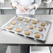 A person wearing gloves is putting cookies in a Chicago Metallic hamburger bun pan.