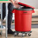 A man using a dolly to open a red Lavex commercial trash can with a black bag inside.