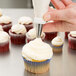 A hand using an Ateco plastic coated canvas pastry bag to frost a cupcake.