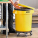 A man opening a yellow Lavex 20 gallon trash can with a lid.