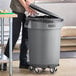 A man using a metal dolly to open a Lavex 32 gallon trash can in a school kitchen.