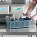 A person in a blue apron putting silverware in a Noble Products grey flatware rack.