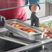 A person in gloves holding a Choice stainless steel steam table pan of food.