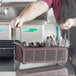 A person holding a brown flatware rack with metal handles full of utensils.