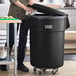 A man standing next to a black Lavex commercial trash can in a professional kitchen.