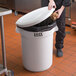 A person putting a white bag in a white Lavex trash can with a lid.