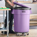 A man using a dolly to move a Lavex purple commercial trash can.