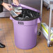 A person putting foil in a purple Lavex 32 gallon trash can with a lid.