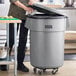 A woman putting a lid on a Lavex 55 gallon gray commercial trash can.