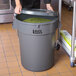 A woman holding a large Lavex gray trash can lid over green food.