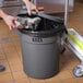 A person putting a bag in a Lavex 20 gallon gray commercial trash can with a lid.