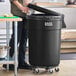 A man standing in a professional kitchen next to a black Lavex commercial trash can.