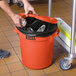 A person putting foil in an orange Lavex trash can.