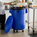 A woman using a dolly to put a can into a blue Lavex commercial trash can.