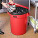 A woman putting foil in a red Lavex round trash can with a plastic wrap on the lid.