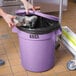 A person putting a bag in a Lavex purple trash can.