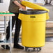 A man opening a yellow Lavex trash can with a dolly lid.