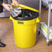 A woman holding a bag of foil puts it in a yellow Lavex trash can with a lid.