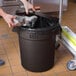 A hand putting a bag of foil in a Lavex brown round commercial trash can.